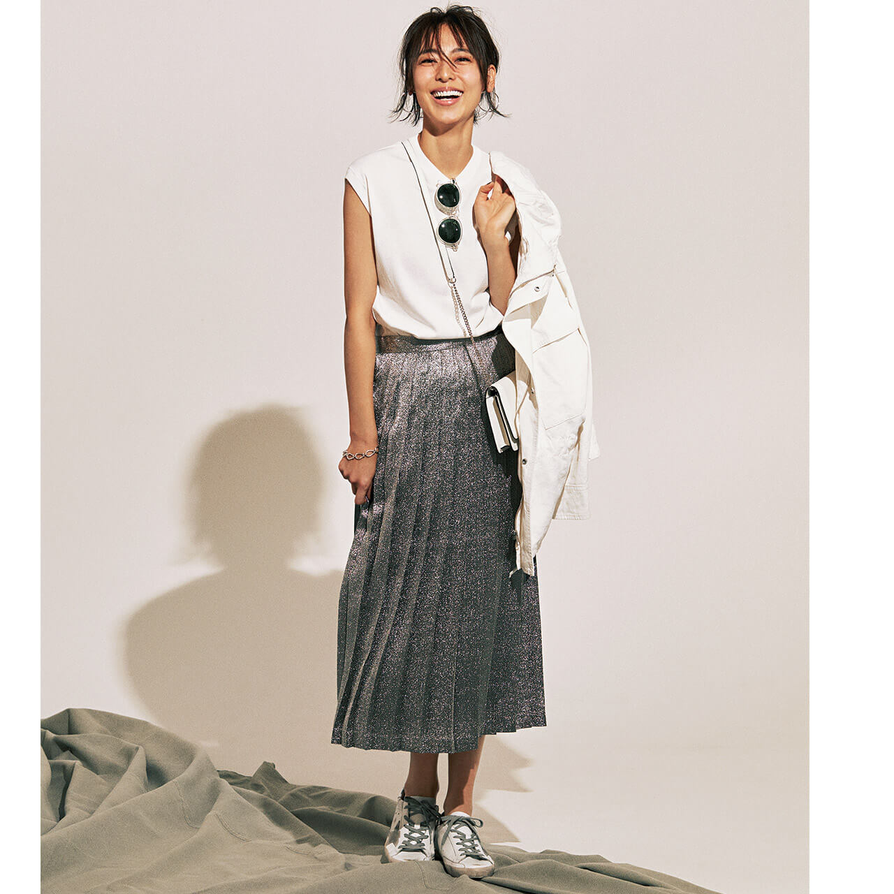 手に持ったジャケット×ニット×シルバーのプリーツスカートコーデを着たモデルの小泉里子さん