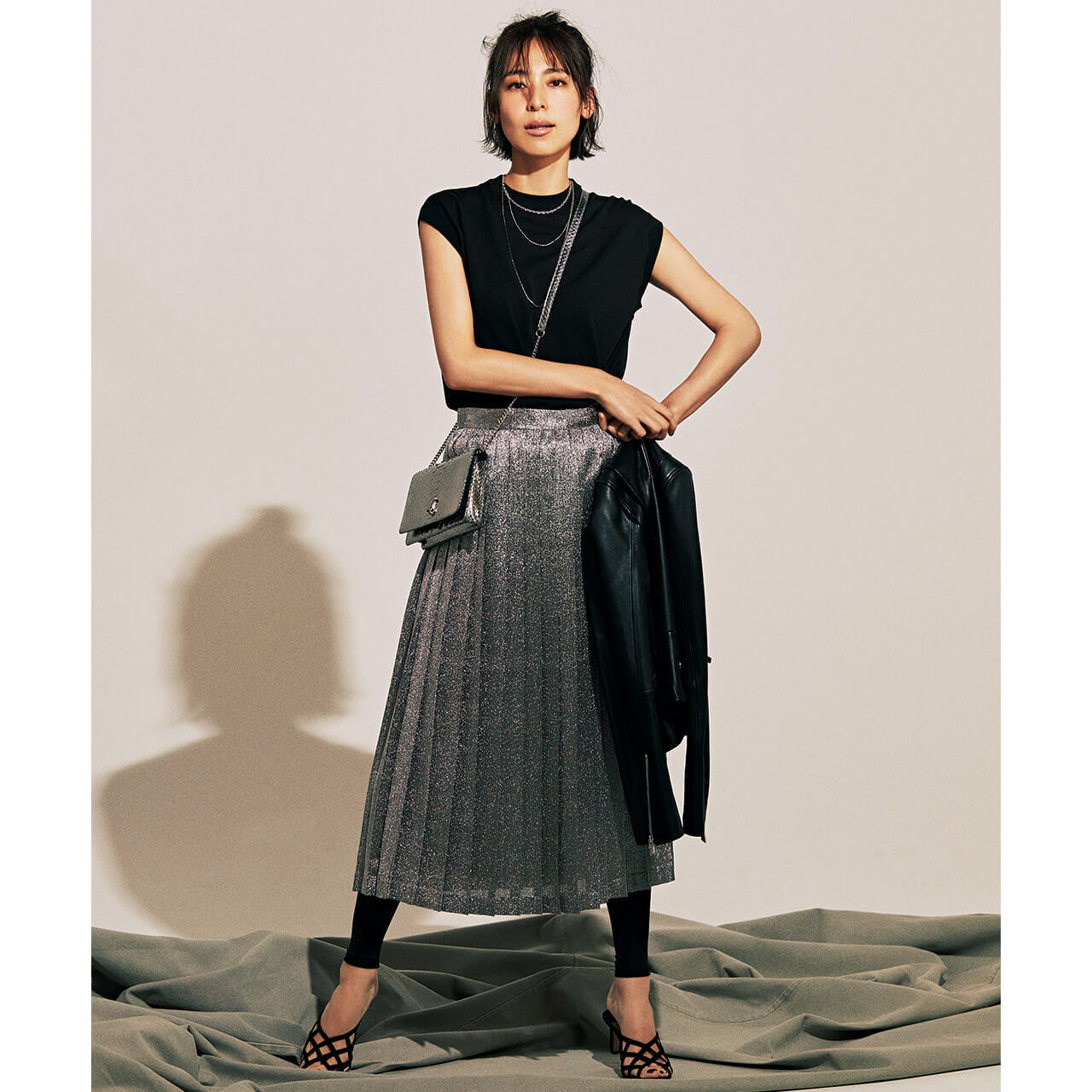 手に持ったジャケット×ニット×シルバーのプリーツスカートコーデを着たモデルの小泉里子さん